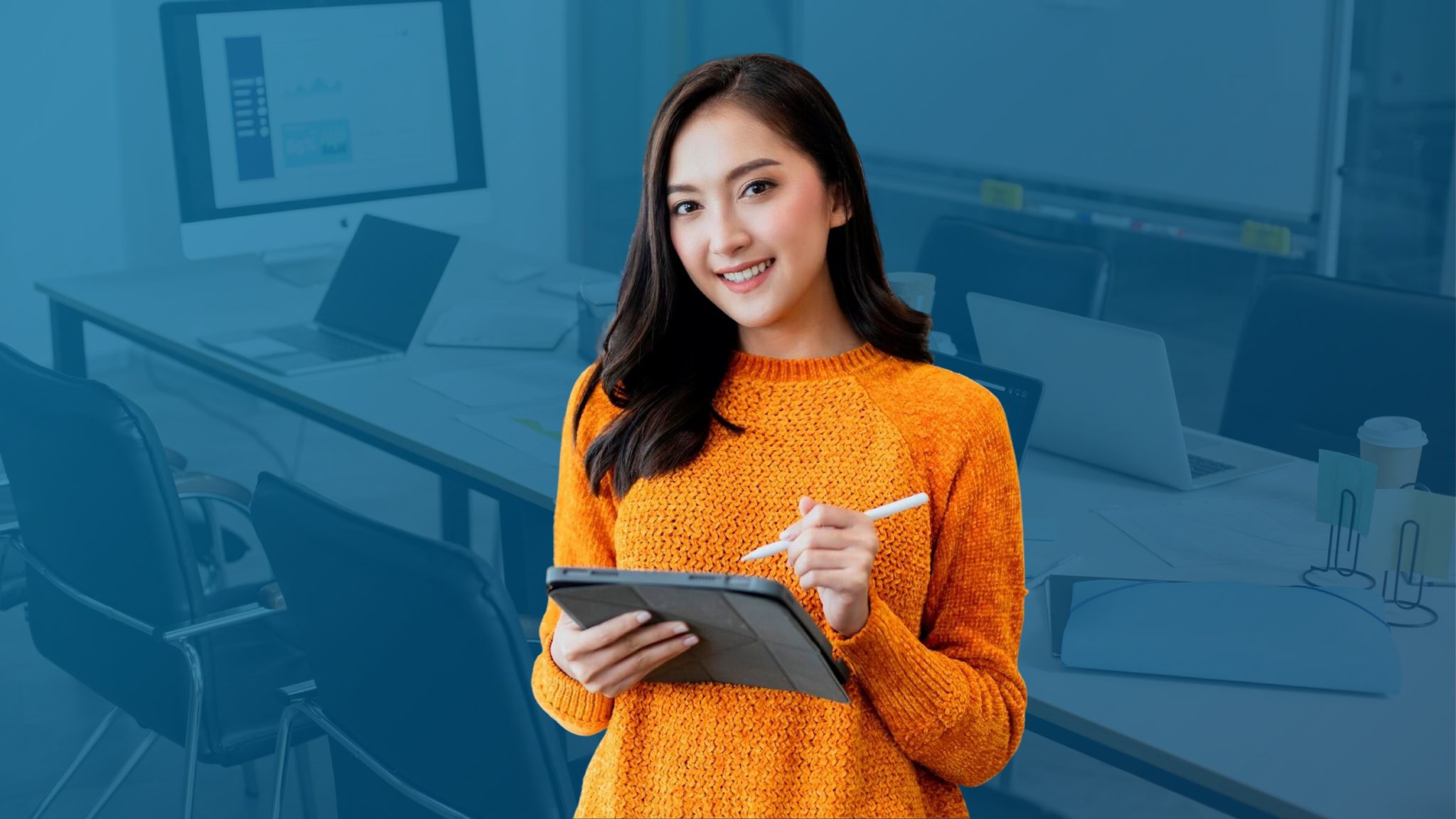 Smiling woman in an orange sweater using a digital tablet, symbolizing team collaboration, workflow automation, and cost efficiency in communication.