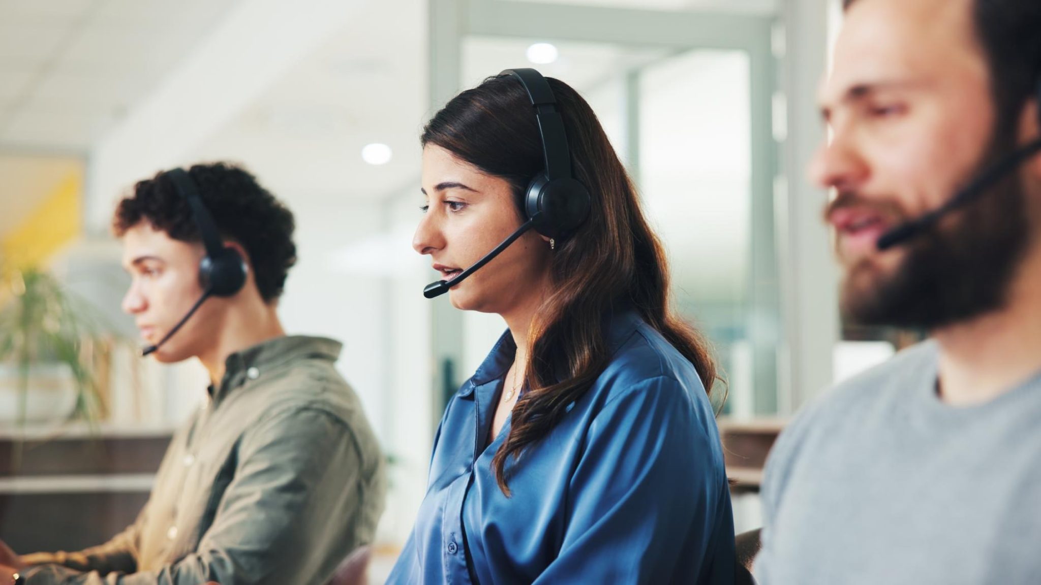 Image of three customer service representatives wearing headsets and assisting callers in an office setting, representing how AI Call Analytics supports team performance, call monitoring, and communication insights.